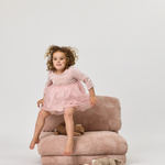 Child in a pink dress sitting on a Rylee Recliner chair with a white background
