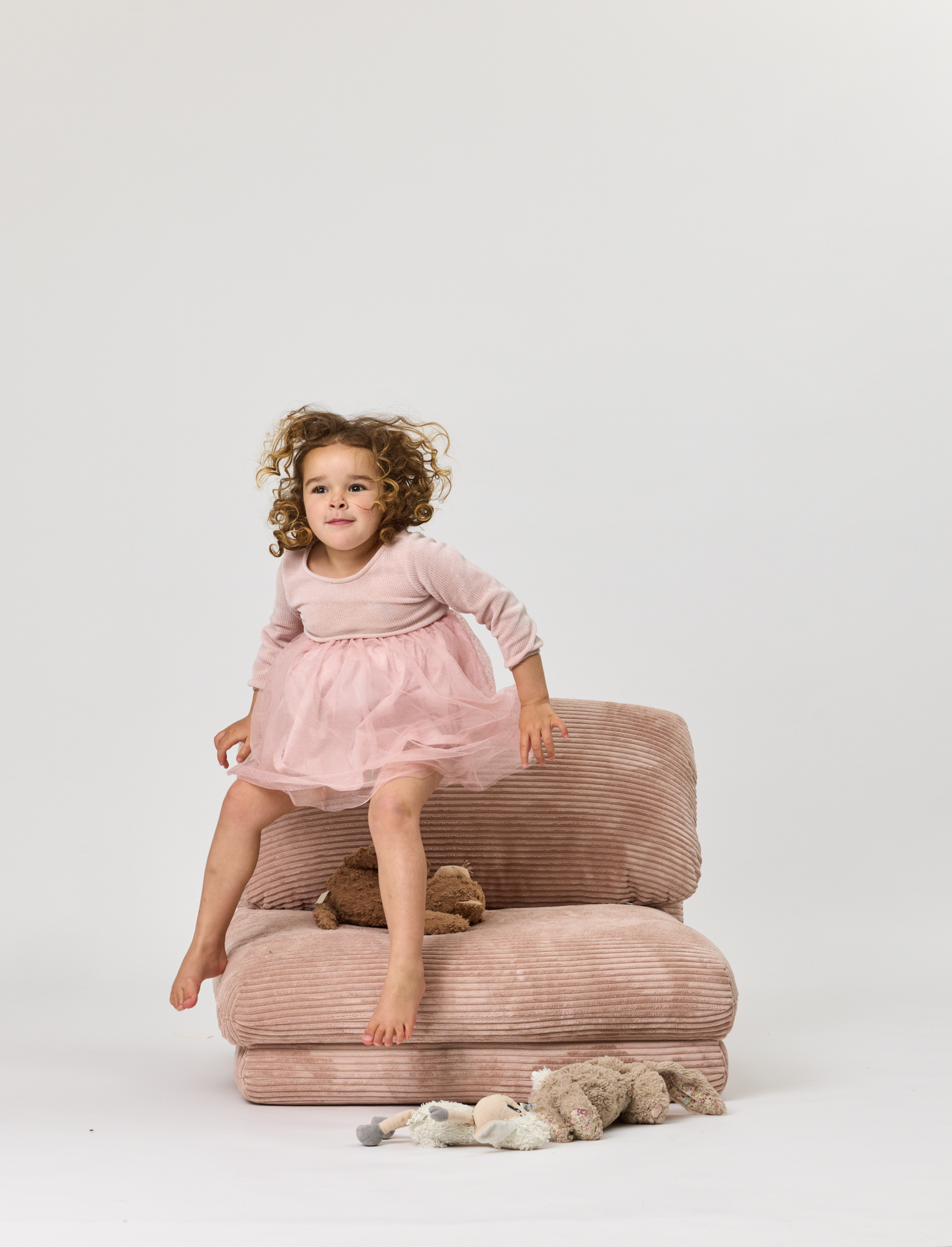 Child in a pink dress sitting on a Rylee Recliner chair with a white background
