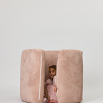 Child peeking out from a pink cushioned playpen on a white background
