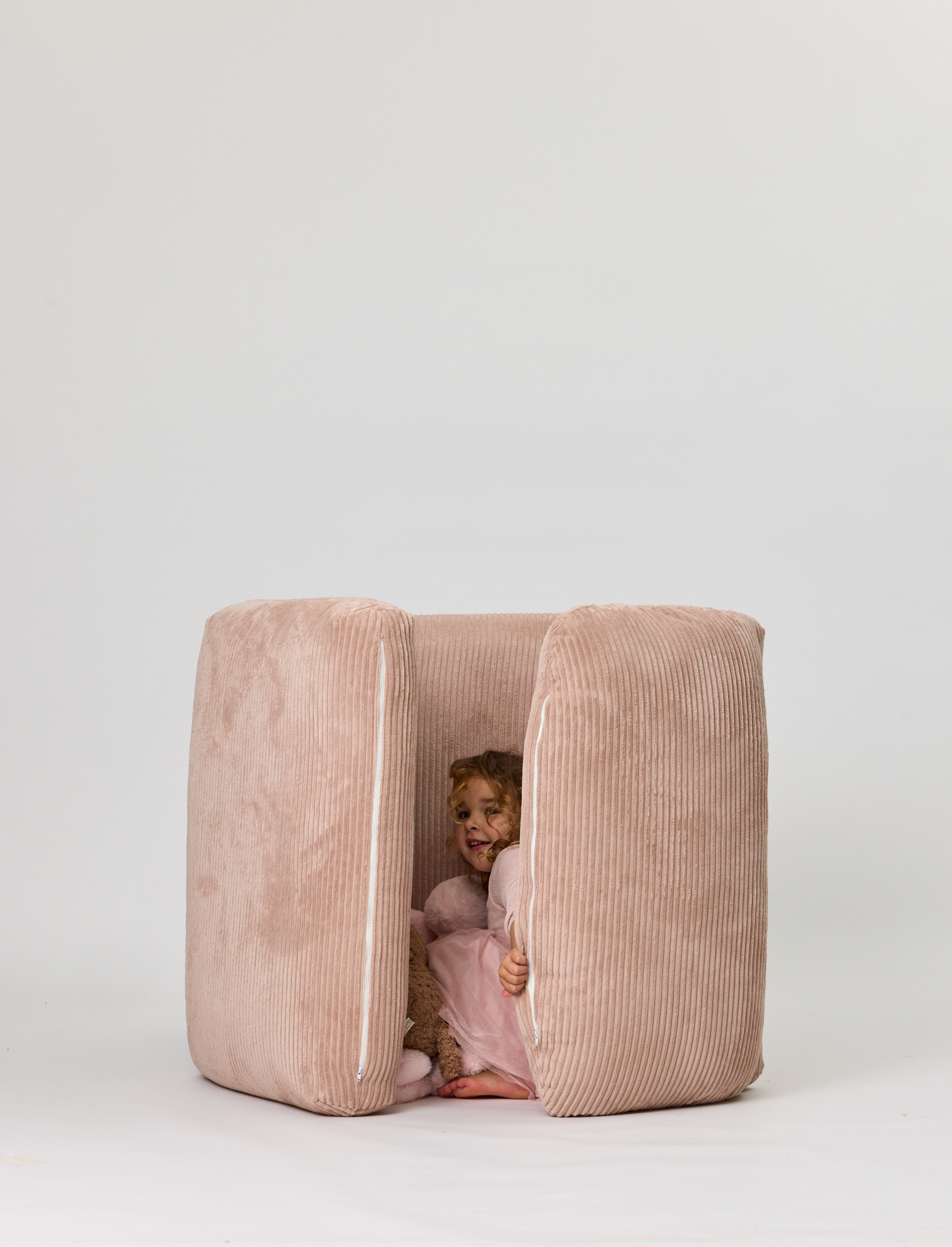 Child peeking out from a pink cushioned playpen on a white background