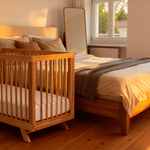 MacKenzie Cot from Cariboo next to a bed in a bedroom with natural light