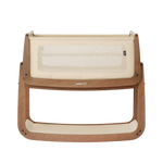 SnüzPod5 baby bassinet with a natural wood frame, cream mesh backrest, and beige fabric lining, shown against a solid white background.