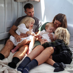Family of four sitting together on a bed with a neutral background